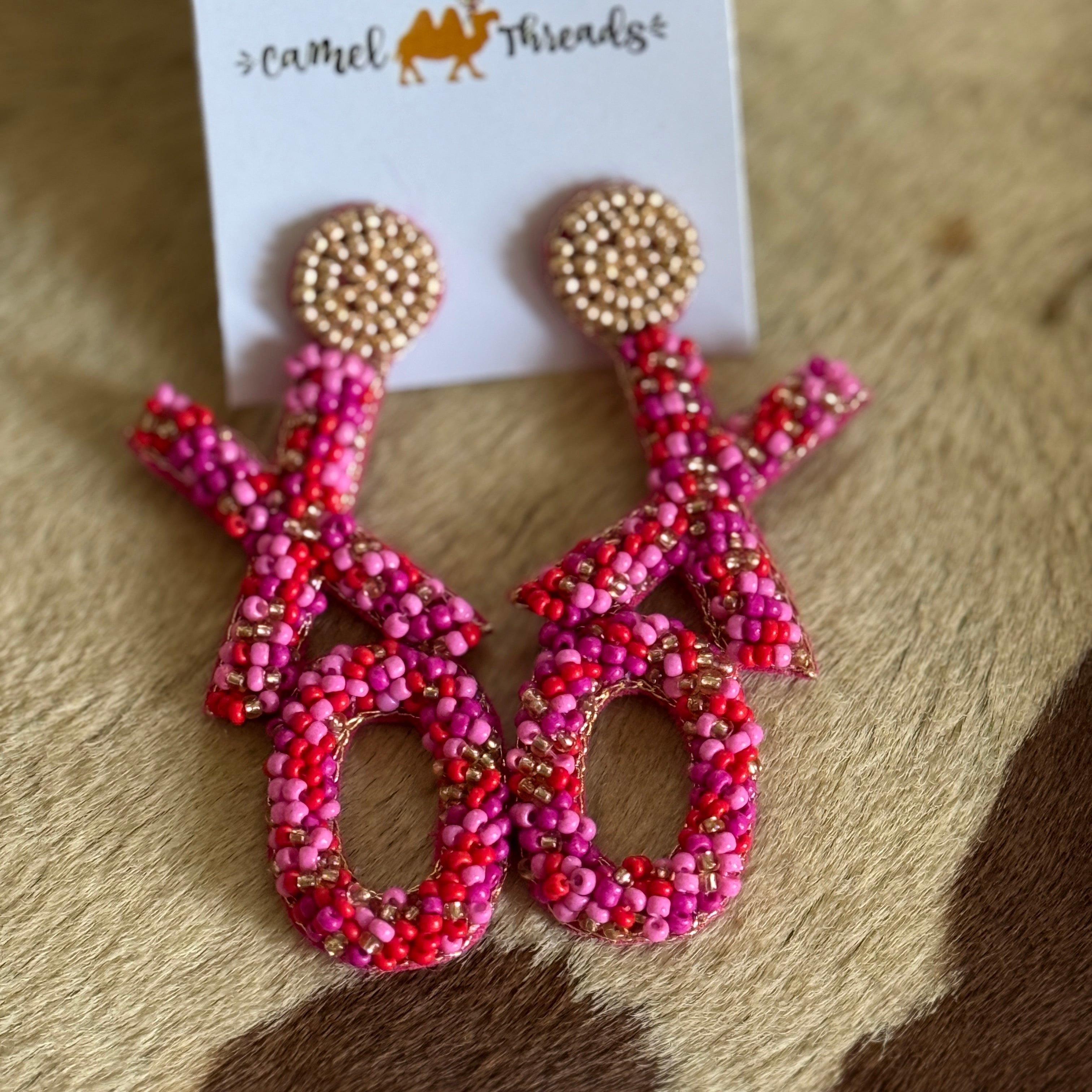 A pair of red and pink beaded XO earrings on a white display card, with the design resembling a heart and an infinity symbol.