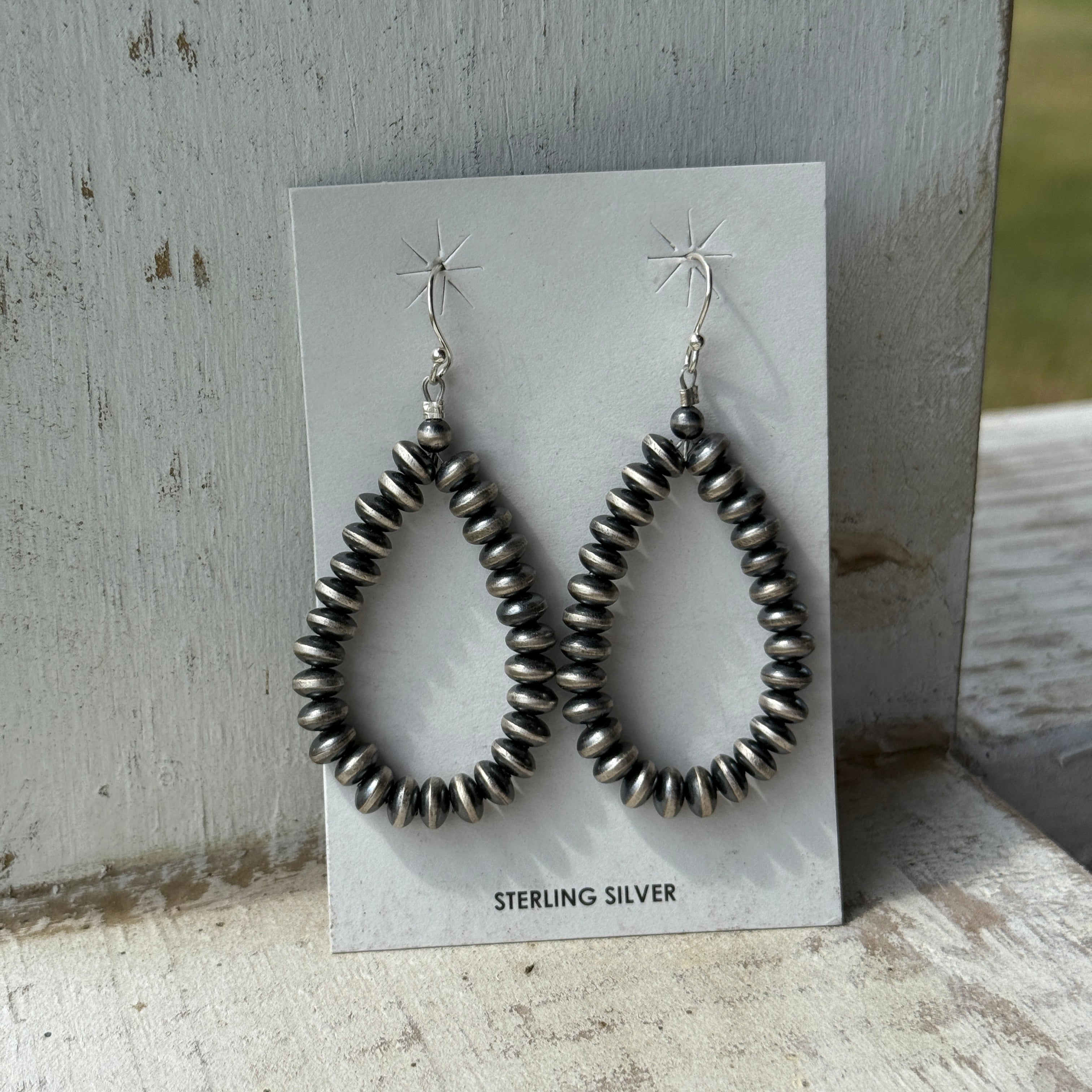 Silver beaded earrings on a card with 'Sterling Silver' text, placed on a textured surface.