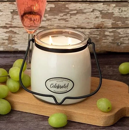 Candle in a glass jar with a decorative handle on a wooden board, surrounded by green grapes.
