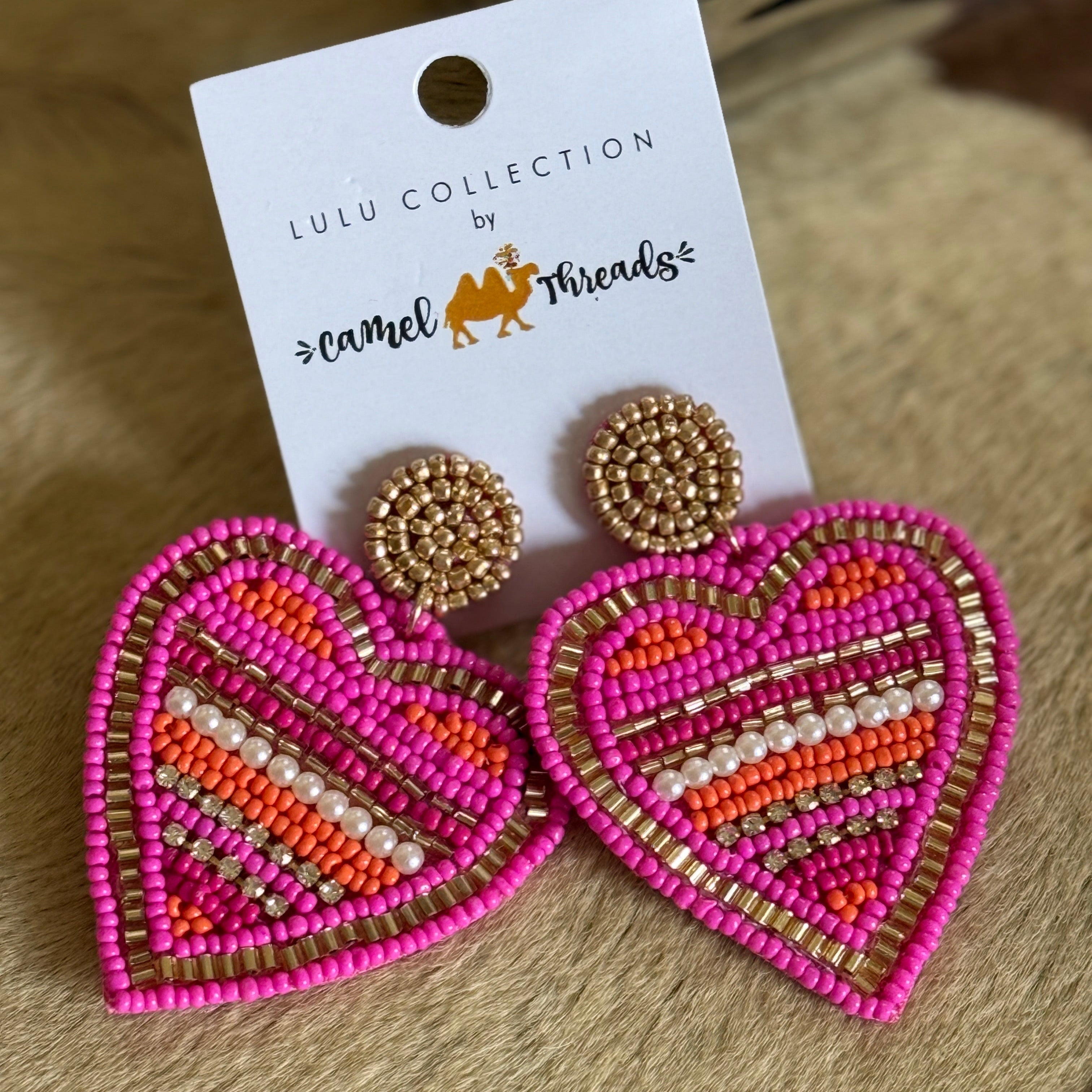 A pair of beaded heart-shaped earrings in pink, orange, and gold, attached to a white card with 'Lulu Collection by LuLu & Friends' printed on it.