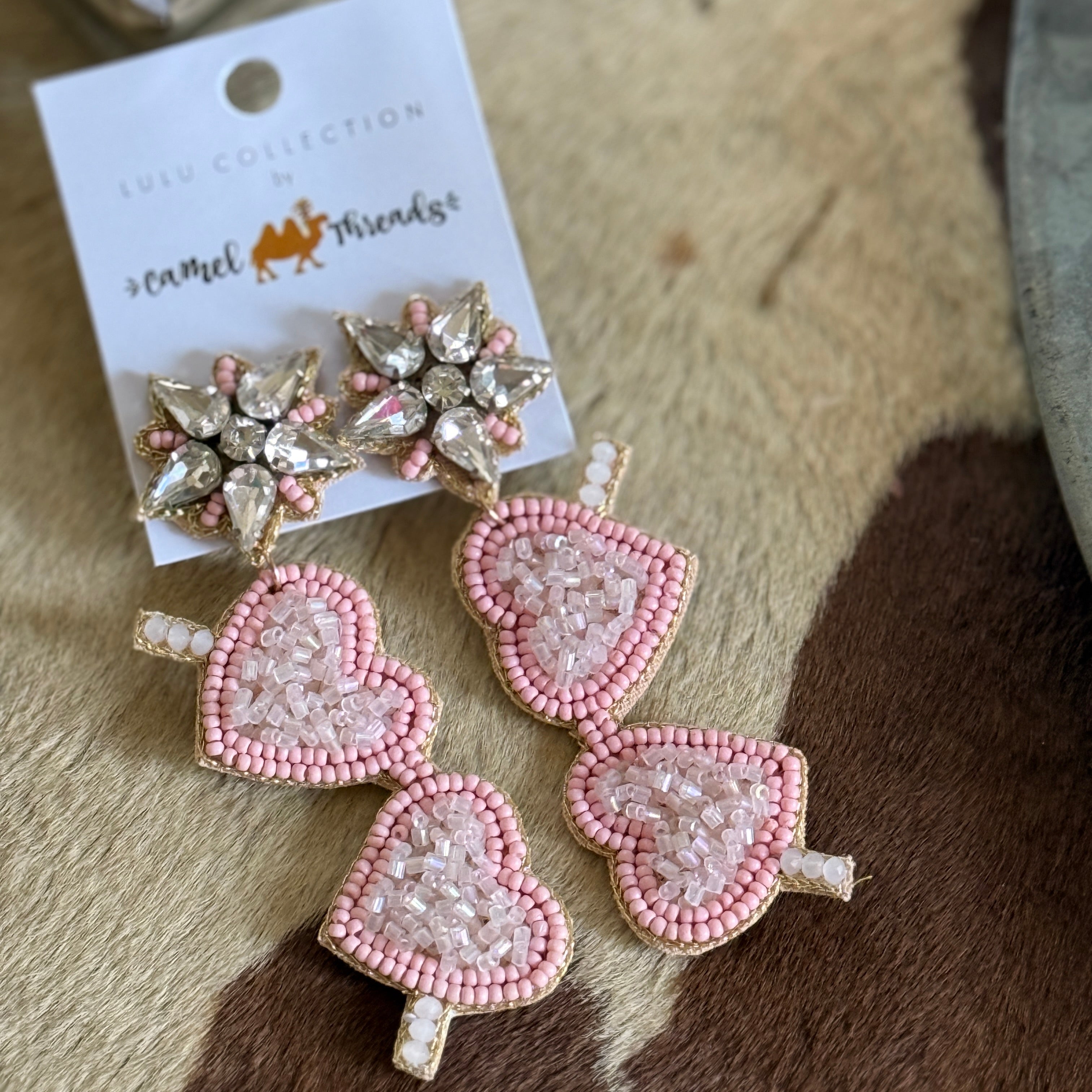 A pair of pink heart-shaped earrings with bead detailing displayed on a card, indicating they are accessories.