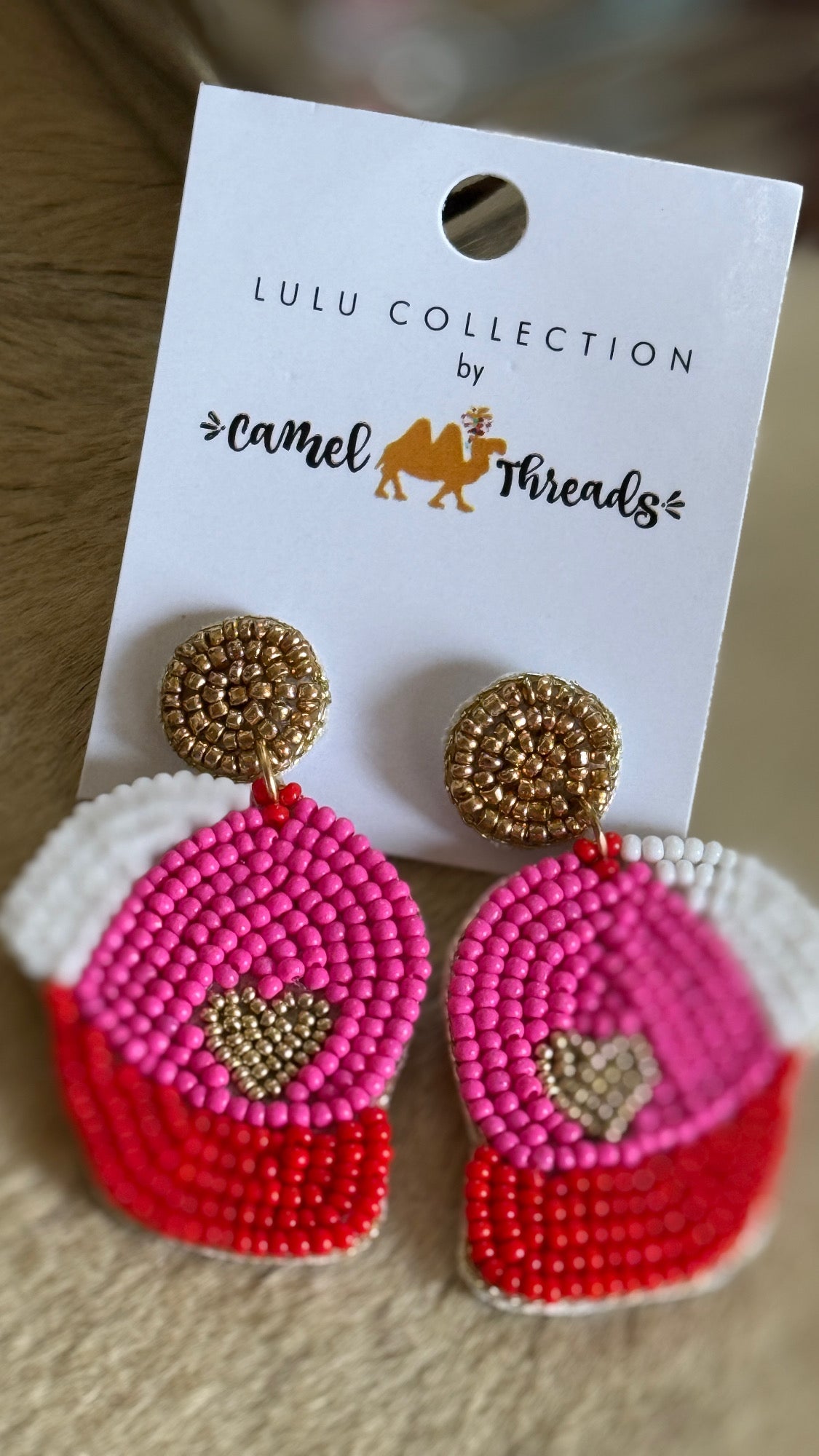 A pair of beaded earrings with a ball cap design featuring a heart, displayed on a white card with the LULU COLLECTION by Camel Threads branding.