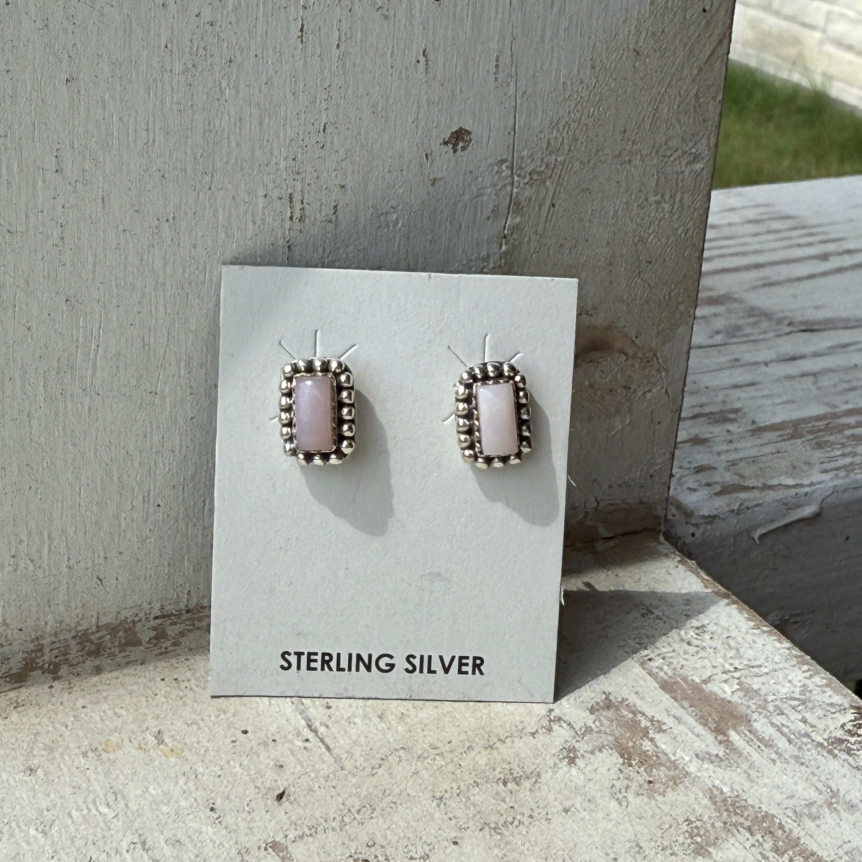 Sterling silver earrings with pink opal on a branded card against a concrete background
