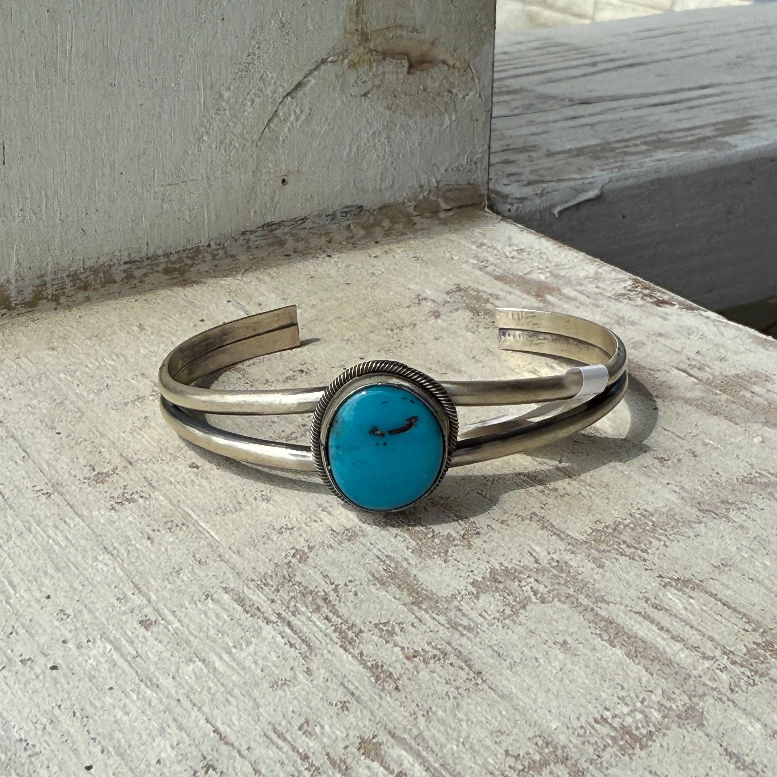 Silver bracelet with a turquoise stone on a textured surface