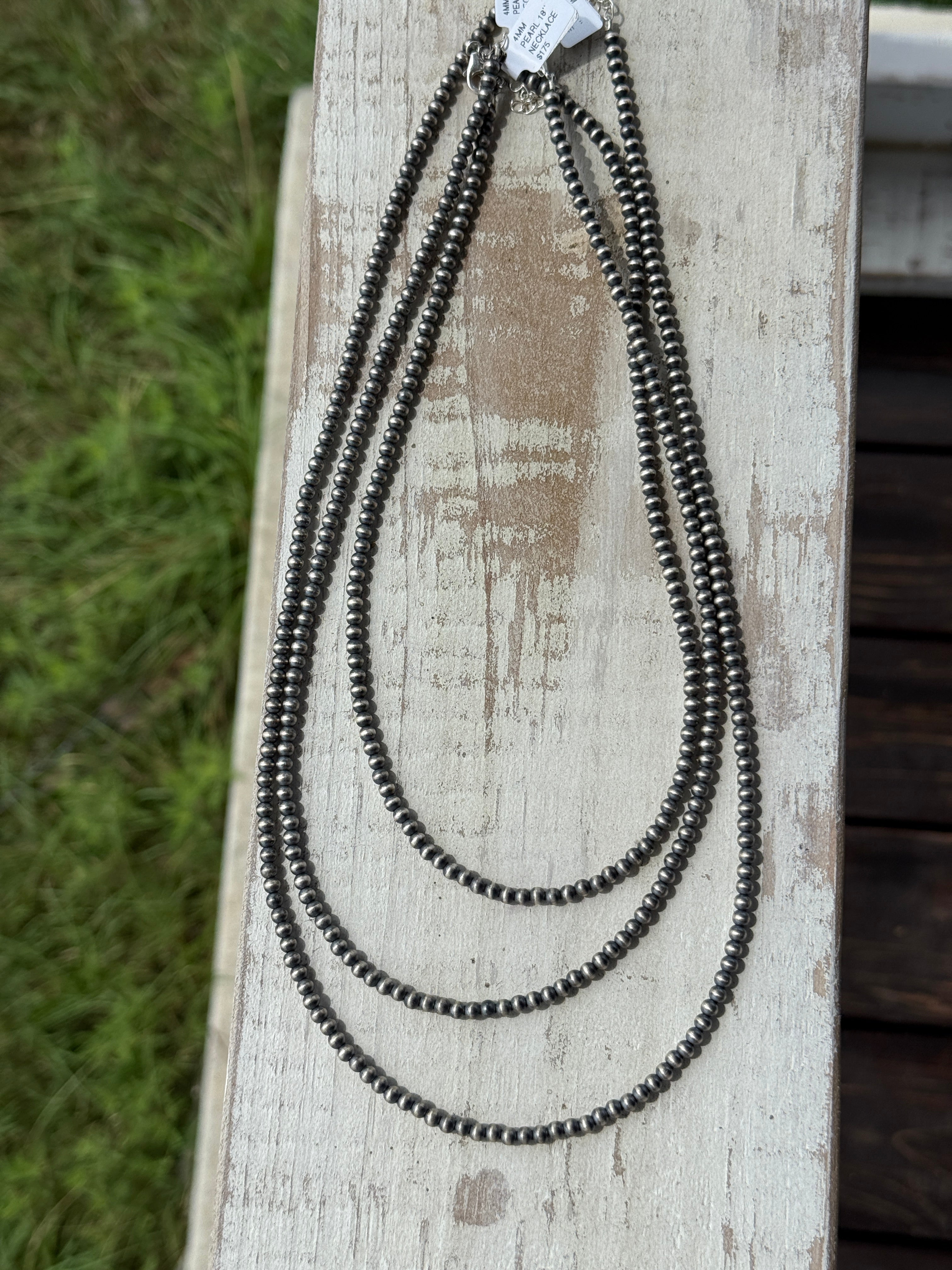 Three navajo pearl necklaces on a wooden surface with grass in the background