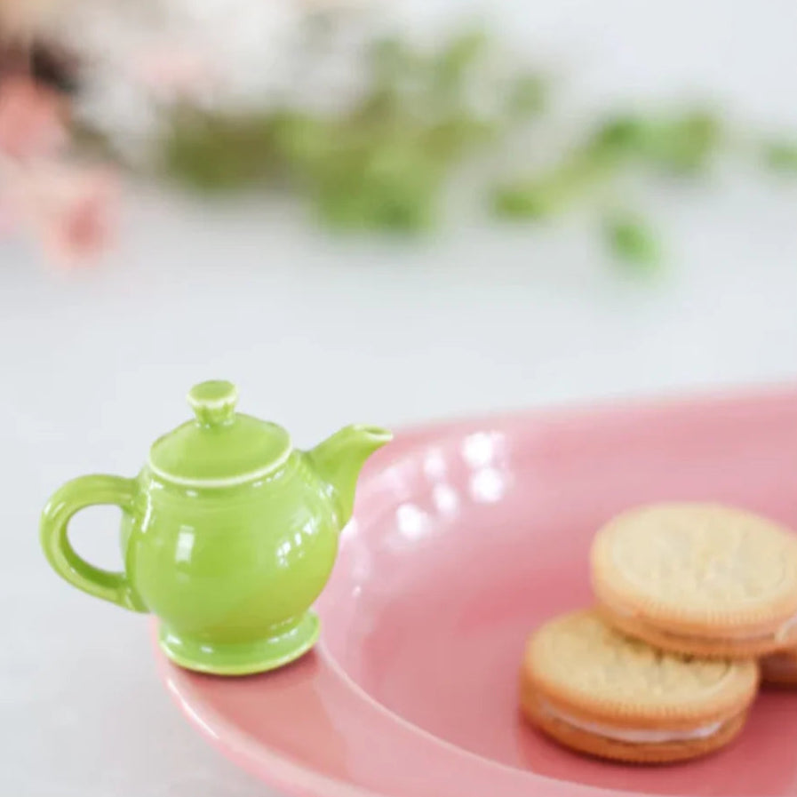 Green teapot on a pink plate with cookies, blurred background