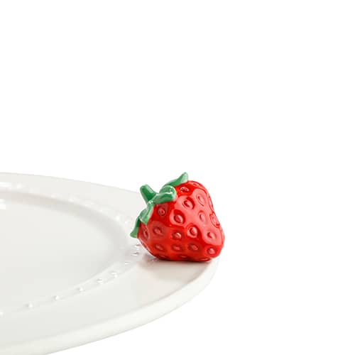 A ceramic red strawberry figurine designed for use as a dessert garnish, placed on a white plate against a white background.